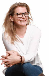 Anja Niekerken sitzt, hat die Beine übergeschlagen und lächelt an der Kamera vorbei