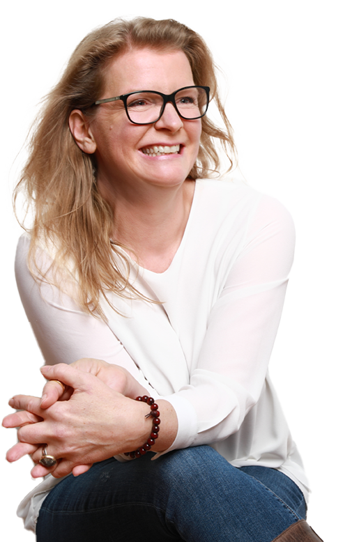 Anja-Freisteller-gespiegelt Anja Niekerken sitzt, hat die Beine übergeschlagen und lächelt an der Kamera vorbei
